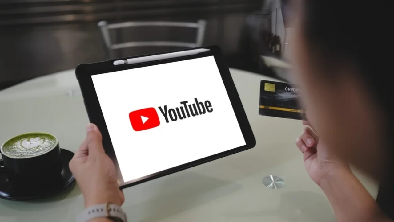 YouTube लोगो के साथ टैबलेट और क्रेडिट कार्ड पकड़े व्यक्ति